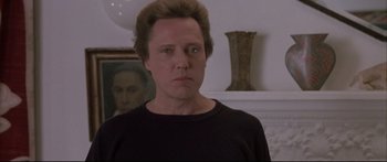 Movie still from “Communion” (1989), directed by Philippe Mora – A man in black shirt standing in front of a painting; Close Up shot, Low angle