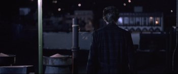 Movie still from “Communion” (1989), directed by Philippe Mora – A man in a black jacket standing next to a pole; Wide shot, Over the shoulder angle