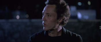 Movie still from “Communion” (1989), directed by Philippe Mora – A person wearing a black shirt; Close Up shot, Low angle