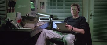 Movie still from “Communion” (1989), directed by Philippe Mora – A man sitting in front of a computer monitor; Medium shot, Low angle