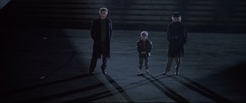 Movie still from “Communion” (1989), directed by Philippe Mora – A group of people standing in a parking lot at night; Wide shot, High angle