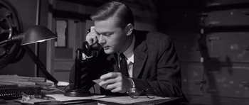 Movie still from “Compulsion” (1959), directed by Richard Fleischer – A man sitting at a desk holding a piece of paper and talking on a phone; Close Up shot, Low angle
