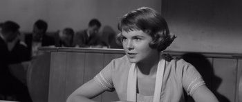 Movie still from “Compulsion” (1959), directed by Richard Fleischer – A woman sitting at a table in front of other people; Close Up shot, Over the shoulder angle