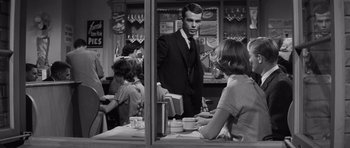 Movie still from “Compulsion” (1959), directed by Richard Fleischer – A man standing at a counter in front of a woman; Medium shot, Over the shoulder angle