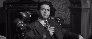 Movie still from “Compulsion” (1959), directed by Richard Fleischer – Black and white photograph of a man in a suit holding a glass; Close Up shot, Low angle