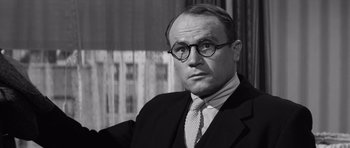 Movie still from “Compulsion” (1959), directed by Richard Fleischer – A man in a suit and tie wearing glasses; Close Up shot, Low angle