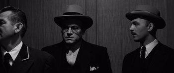 Movie still from “Compulsion” (1959), directed by Richard Fleischer – A black and white photo of a man in a suit and hat; Close Up shot, Low angle