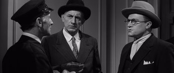 Movie still from “Compulsion” (1959), directed by Richard Fleischer – A man in a suit and hat standing next to two other men; Close Up shot, Over the shoulder angle