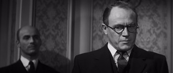 Movie still from “Compulsion” (1959), directed by Richard Fleischer – A man in a suit and tie standing in front of a wall; Close Up shot, Low angle