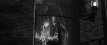 Movie still from “Compulsion” (1959), directed by Richard Fleischer – A black and white photo of a man standing in front of a fire; Medium shot, Low angle