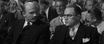 Movie still from “Compulsion” (1959), directed by Richard Fleischer – A black - and - white photo of two men in suits and ties; Medium shot, Over the shoulder angle