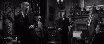 Movie still from “Compulsion” (1959), directed by Richard Fleischer – A man in a suit and tie sitting in a chair; Medium shot, Low angle