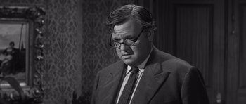 Movie still from “Compulsion” (1959), directed by Richard Fleischer – An older man wearing a suit and glasses; Close Up shot, Over the shoulder angle