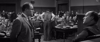 Movie still from “Compulsion” (1959), directed by Richard Fleischer – An old photo of a man speaking in a court room; Medium shot, Over the shoulder angle