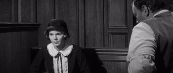 Movie still from “Compulsion” (1959), directed by Richard Fleischer – A woman sitting in front of a wooden wall wearing a hat; Close Up shot, High angle