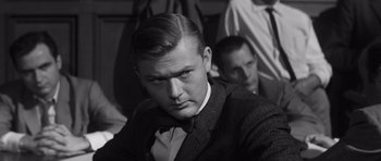 Movie still from “Compulsion” (1959), directed by Richard Fleischer – A man in a suit and bow tie looking at the camera; Close Up shot, Over the shoulder angle