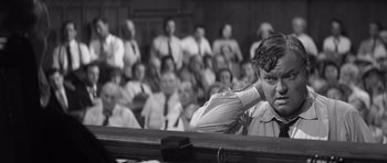 Movie still from “Compulsion” (1959), directed by Richard Fleischer – A black - and - white photo of a man in front of an audience; Medium shot, Low angle