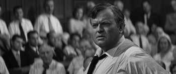 Movie still from “Compulsion” (1959), directed by Richard Fleischer – An old photo of a man in a crowd of people; Close Up shot, Over the shoulder angle