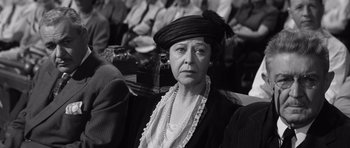 Movie still from “Compulsion” (1959), directed by Richard Fleischer – An older woman wearing a hat and a necklace; Close Up shot, Over the shoulder angle