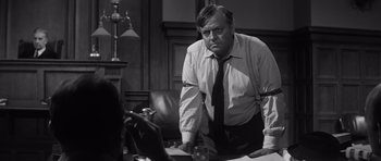 Movie still from “Compulsion” (1959), directed by Richard Fleischer – A man in a tie is standing in front of a table; Medium shot, Over the shoulder angle