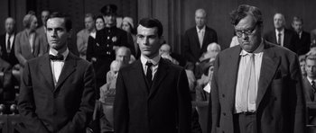 Movie still from “Compulsion” (1959), directed by Richard Fleischer – Black and white photograph of a man in a suit and tie in front of a group of people; Medium shot, Low angle
