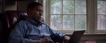 Movie still from “The Equalizer 2” (2018), directed by Antoine Fuqua – A man sitting in front of a laptop computer in front of a window; Medium shot, Low angle