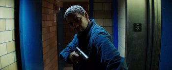 Movie still from “The Equalizer 2” (2018), directed by Antoine Fuqua – A man holding a gun while standing next to a wall; Medium shot, Low angle
