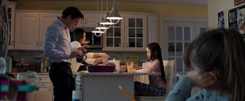 Movie still from “The Equalizer 2” (2018), directed by Antoine Fuqua – A girl sitting at a kitchen table with her family; Medium shot, Over the shoulder angle
