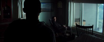 Movie still from “The Equalizer 2” (2018), directed by Antoine Fuqua – A man sitting in a chair in front of a window; Medium shot, Over the shoulder angle