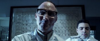 Movie still from “Confessions of a Dangerous Mind” (2002), directed by George Clooney – A man wearing a lab coat and glasses in front of a periodic table of the elements; Close Up shot, Low angle
