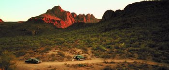 Movie still from “Confessions of a Dangerous Mind” (2002), directed by George Clooney – A car parked on the side of a road in the desert; Extreme Wide shot, Low angle