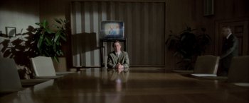 Movie still from “Confessions of a Dangerous Mind” (2002), directed by George Clooney – A man sitting at a table in front of a television; Wide shot, High angle