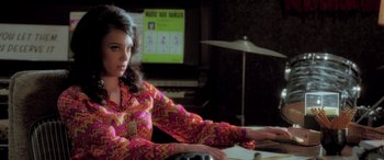 Movie still from “Confessions of a Dangerous Mind” (2002), directed by George Clooney – A woman in a pink and yellow shirt sitting in front of a piano; Medium shot, High angle
