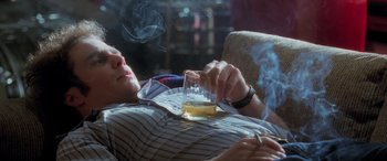 Movie still from “Confessions of a Dangerous Mind” (2002), directed by George Clooney – A man smoking a cigarette while holding a glass of alcohol; Medium shot, High angle