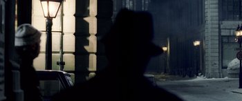 Movie still from “Confessions of a Dangerous Mind” (2002), directed by George Clooney – A man wearing a black hat standing in front of a building; Medium shot, Over the shoulder angle