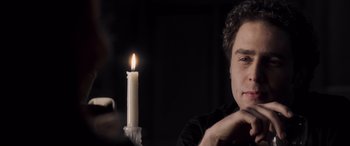 Movie still from “Confessions of a Dangerous Mind” (2002), directed by George Clooney – A man sitting in front of a lit candle in a dark room; Close Up shot, Over the shoulder angle