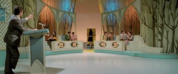 Movie still from “Confessions of a Dangerous Mind” (2002), directed by George Clooney – A group of people sitting in front of a stage; Extreme Wide shot, High angle