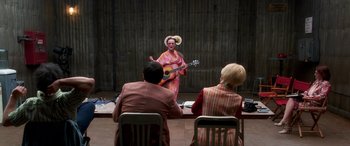 Movie still from “Confessions of a Dangerous Mind” (2002), directed by George Clooney – A woman in a colorful dress playing a guitar; Wide shot, Over the shoulder angle