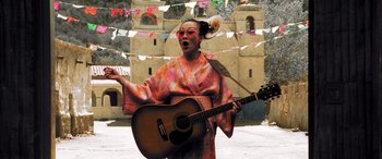 Movie still from “Confessions of a Dangerous Mind” (2002), directed by George Clooney – A woman in a kimono is playing a guitar; Medium shot, Low angle
