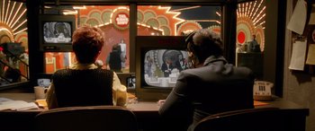 Movie still from “Confessions of a Dangerous Mind” (2002), directed by George Clooney – Two people sitting in front of a television; Wide shot, Over the shoulder angle