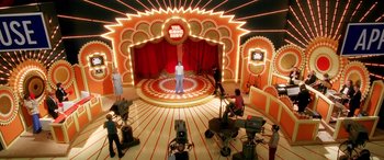 Movie still from “Confessions of a Dangerous Mind” (2002), directed by George Clooney – A man standing in front of an audience in front of lights; Wide shot, High angle