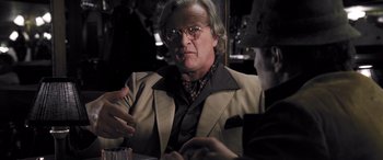 Movie still from “Confessions of a Dangerous Mind” (2002), directed by George Clooney – An older man sitting at a table with a glass of wine; Close Up shot, Over the shoulder angle