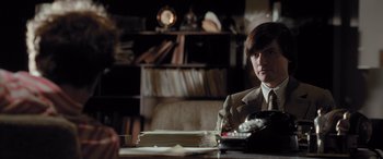 Movie still from “Confessions of a Dangerous Mind” (2002), directed by George Clooney – A man sitting at a table in front of papers; Medium shot, Over the shoulder angle