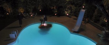 Movie still from “Confessions of a Dangerous Mind” (2002), directed by George Clooney – A man sitting on the edge of a swimming pool at night; Extreme Wide shot, Overhead angle