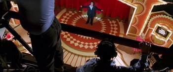 Movie still from “Confessions of a Dangerous Mind” (2002), directed by George Clooney – A man standing on a stage in front of a camera; Wide shot, High angle