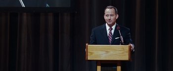 Movie still from “Confessions of a Shopaholic” (2009), directed by P.J. Hogan – A man standing at a podium with a microphone; Medium shot, Over the shoulder angle