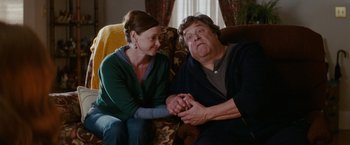 Movie still from “Confessions of a Shopaholic” (2009), directed by P.J. Hogan – A man and a woman sitting on a couch holding hands; Medium shot, Over the shoulder angle