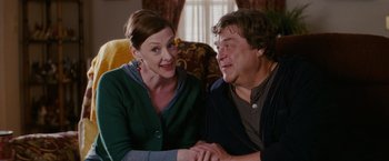 Movie still from “Confessions of a Shopaholic” (2009), directed by P.J. Hogan – A man and a woman sitting on a couch holding hands; Medium shot, Over the shoulder angle