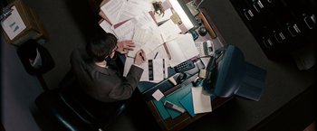 Movie still from “Confessions of a Shopaholic” (2009), directed by P.J. Hogan – A man sitting at a desk writing on a piece of paper; Medium shot, Overhead angle