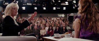 Movie still from “Confessions of a Shopaholic” (2009), directed by P.J. Hogan – A group of people sitting in front of an audience; Medium shot, Over the shoulder angle